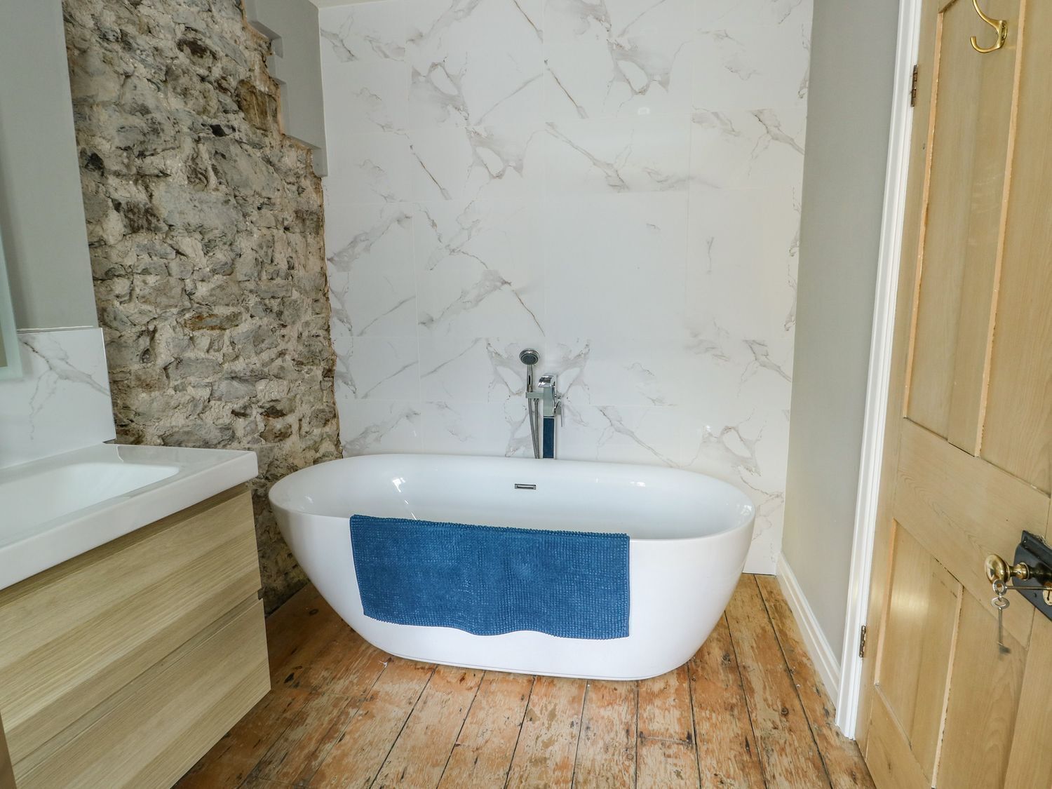 Un baño con una bañera independiente, suelo de madera, pared de piedra y puerta de madera.