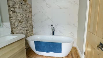 Un baño con una bañera independiente, suelo de madera, pared de piedra y puerta de madera.