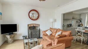 A living room with a leather sofa, a television, a fireplace, and a dining area with a table and chairs. - Tri Raglan Mawr (Beaumaris)