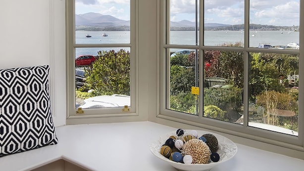 A bay window with a view of a lake, boats, and mountains. - Tri Raglan Mawr (Beaumaris)