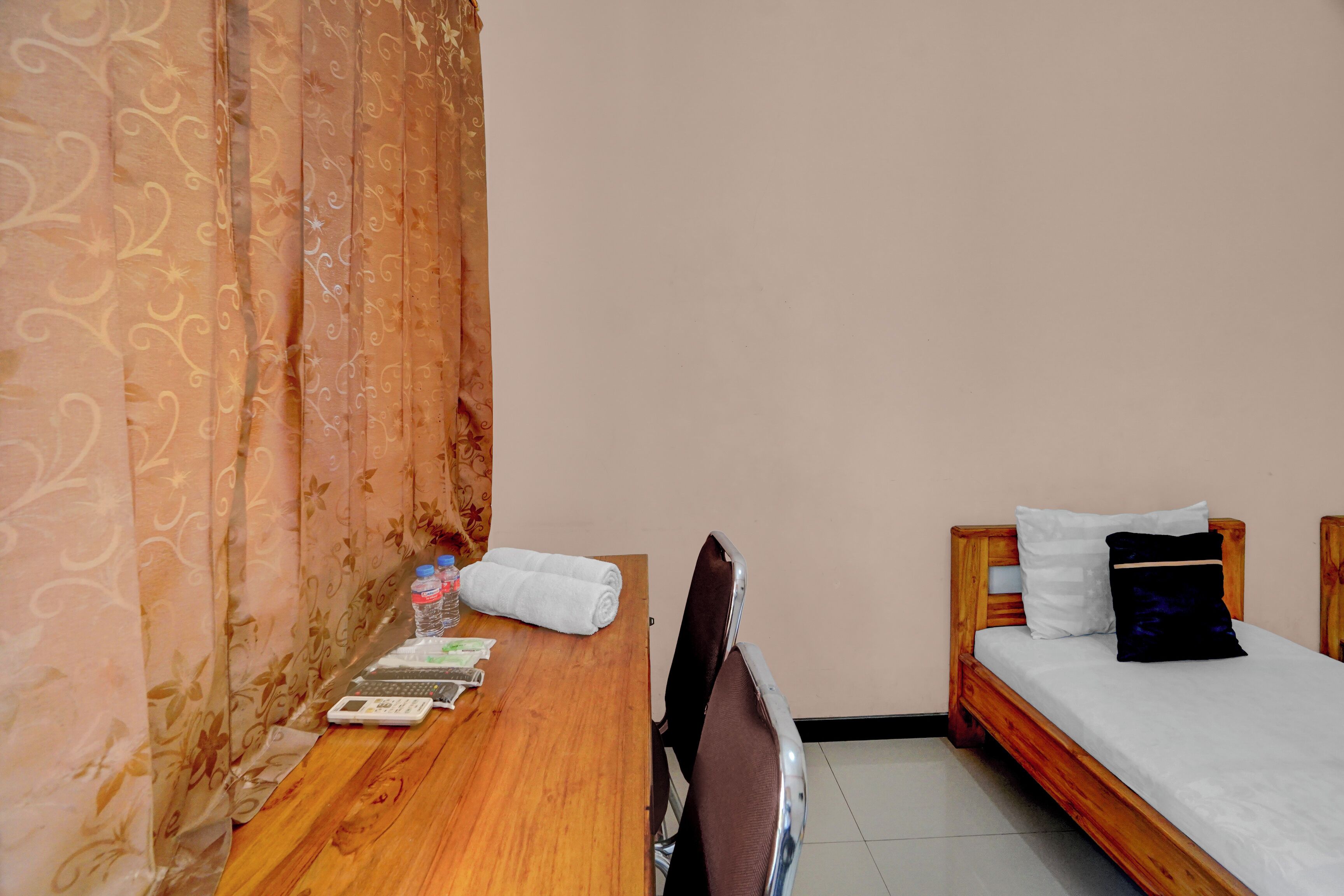 A room with a wooden bed, a wooden desk, and a chair. There are towels, a bottle, and a tissue box on the desk.