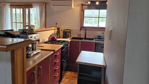 A compact kitchen with wooden cabinets, a gas stove, a sink, and a window with curtains. - Cottage in beautiful Blue Mountains (Mount Victoria)