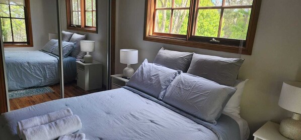 Une chambre à coucher avec un grand lit, deux tables de chevet, un miroir et des fenêtres donnant sur un paysage verdoyant.