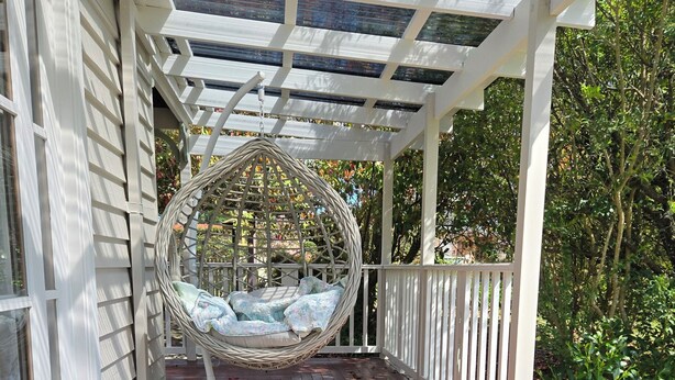 A wooden deck with a hanging swing chair and a white hose on the floor. - Cottage in beautiful Blue Mountains (Mount Victoria)