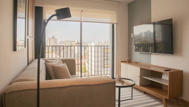 A modern living room with a sofa, a TV, and a balcony with a city view. - w Enchanting 1BR w Balcony in Barranco (Lima)