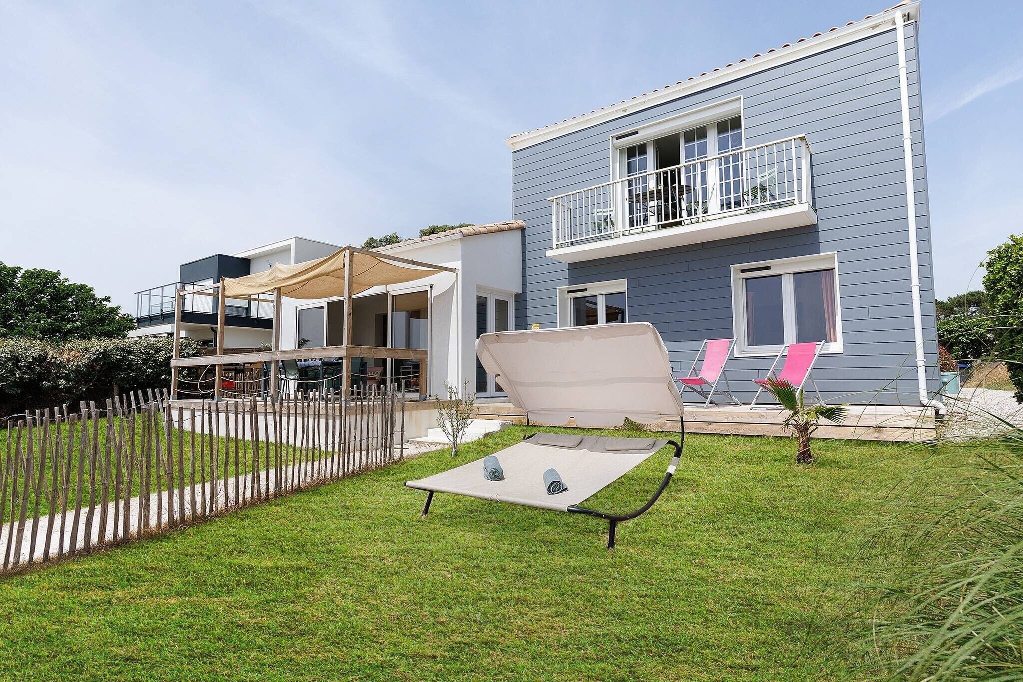 A modern two-story house with a balcony, a covered patio, and a lawn with a sun lounger.
