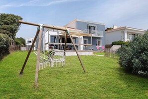 Una casa con un columpio en el patio, una cerca blanca y un edificio azul al fondo.