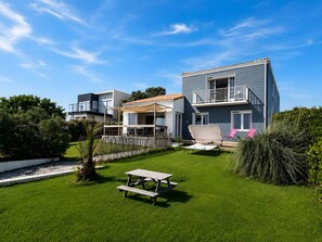 Ein modernes, zweistöckiges Haus mit Balkon, einem grünen Hinterhof und einem Picknicktisch.