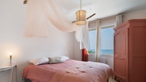 A bedroom with a bed, bedside table, wardrobe, and a view of the sea through the window. - Holiday Home “Les Sables Pailletés 14p” with Sea View, Shared Terrace & Wi-Fi (Les Sables-d'Olonne)