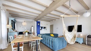 Un comedor con mesa y sillas de madera, sofá azul, hamaca colgante y televisor montado en la pared.