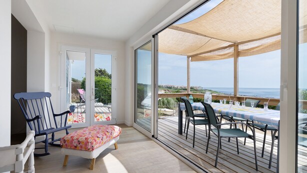 Un balcón con una mesa y sillas, una mecedora y vista al mar.