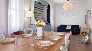 Un comedor con una mesa de madera dispuesta para cuatro, una jarra blanca con flores y un aparador azul al fondo.