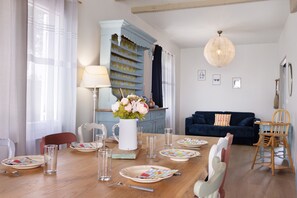 Un comedor con una mesa de madera dispuesta para cuatro, una jarra blanca con flores y un aparador azul al fondo.