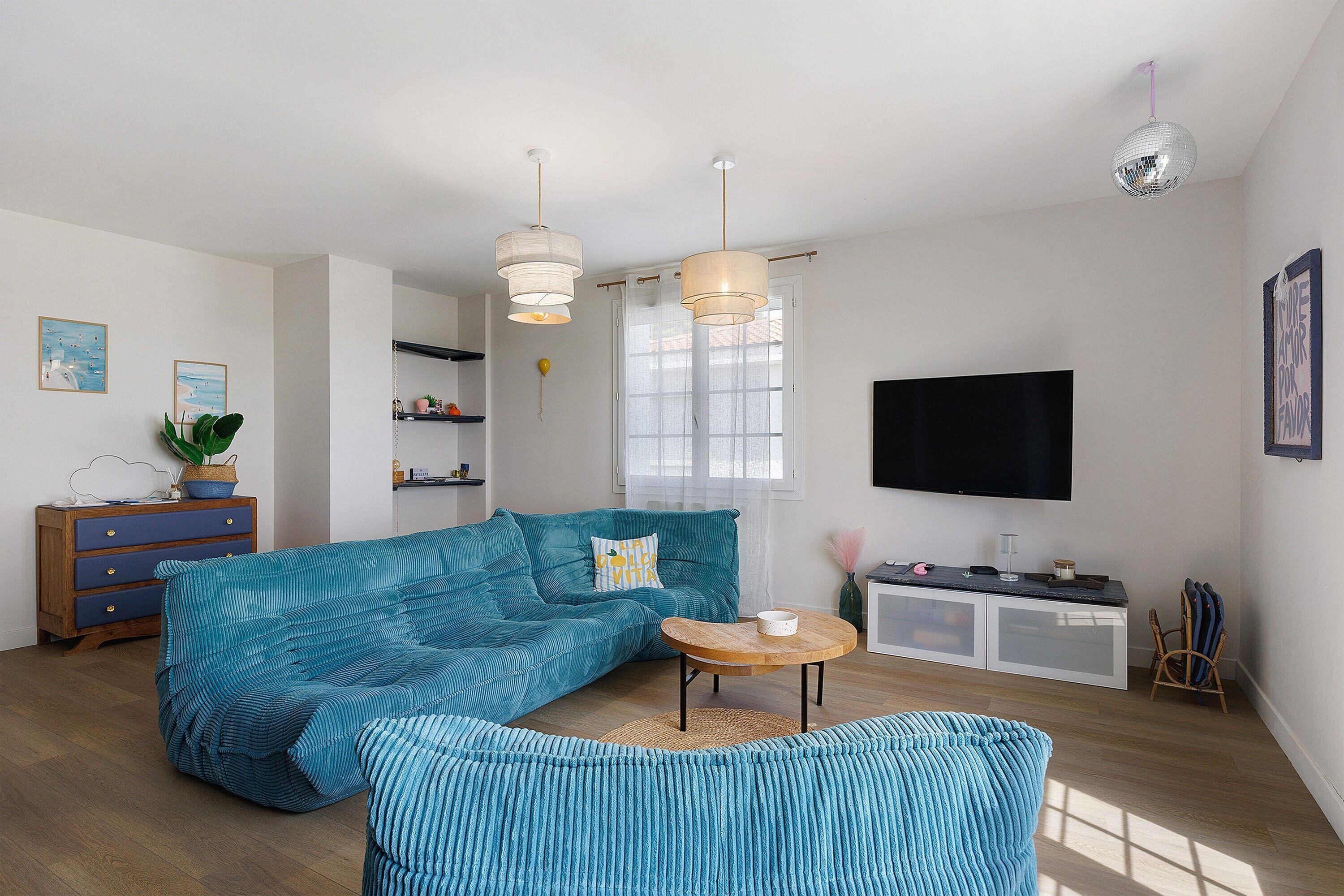 Een woonkamer met een bank, een salontafel, een televisie en hanglampen.