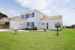 A two-story house with a white exterior, blue shutters, and a tiled roof. - Apartment 'Les Sables Pailletés 4p' with Sea View, Shared Garden and Wi-Fi (Les Sables-d'Olonne)