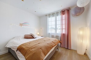 A bedroom with a bed, a window with curtains, a wall with star decorations, and a bedside lamp. - Apartment 'Les Sables Pailletés 4p' with Sea View, Shared Garden and Wi-Fi (Les Sables-d'Olonne)