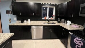 A modern kitchen with dark cabinets, a granite countertop, stainless steel appliances, and a window above the sink. - 3-bedroom house in Miami with large yard, jacuzzi and mango tree’s. (Miami)