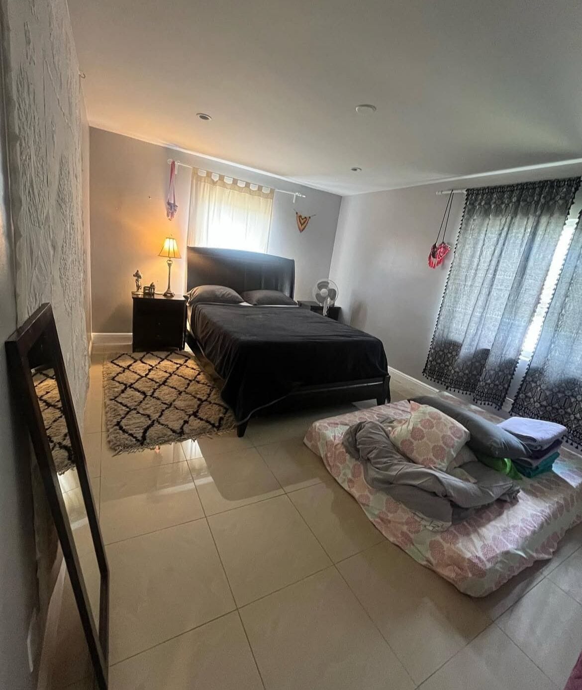 A bedroom with a bed, bedside table, lamp, and a window with curtains.