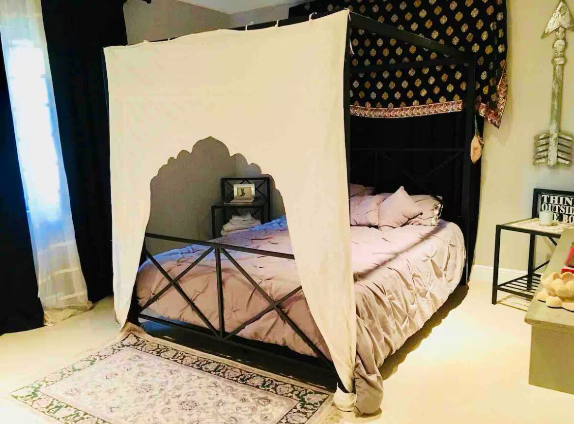A bed with a canopy, a nightstand with a framed picture, and a small table with a sign.