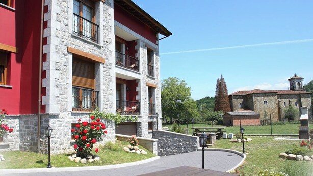 A multi-story building with stone and red exterior walls, a balcony, and a paved area with picnic tables. - Rural Apartments La Viña (Apartment number 6) (Cangas de Onis)