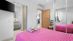 Ein Schlafzimmer mit Bett, Schreibtisch, Stuhl, Fernseher und einem durchgehenden Türspalte sichtbaren Badezimmer.
