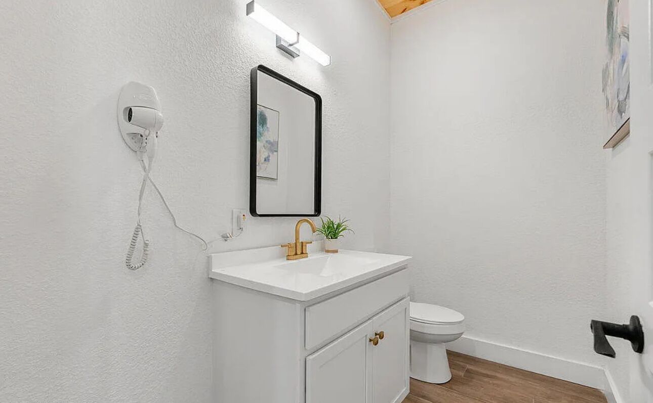 A bathroom with a white sink, a mirror, a toilet, and a security camera.