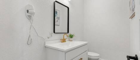 A bathroom with a white sink, a mirror, a toilet, and a security camera.