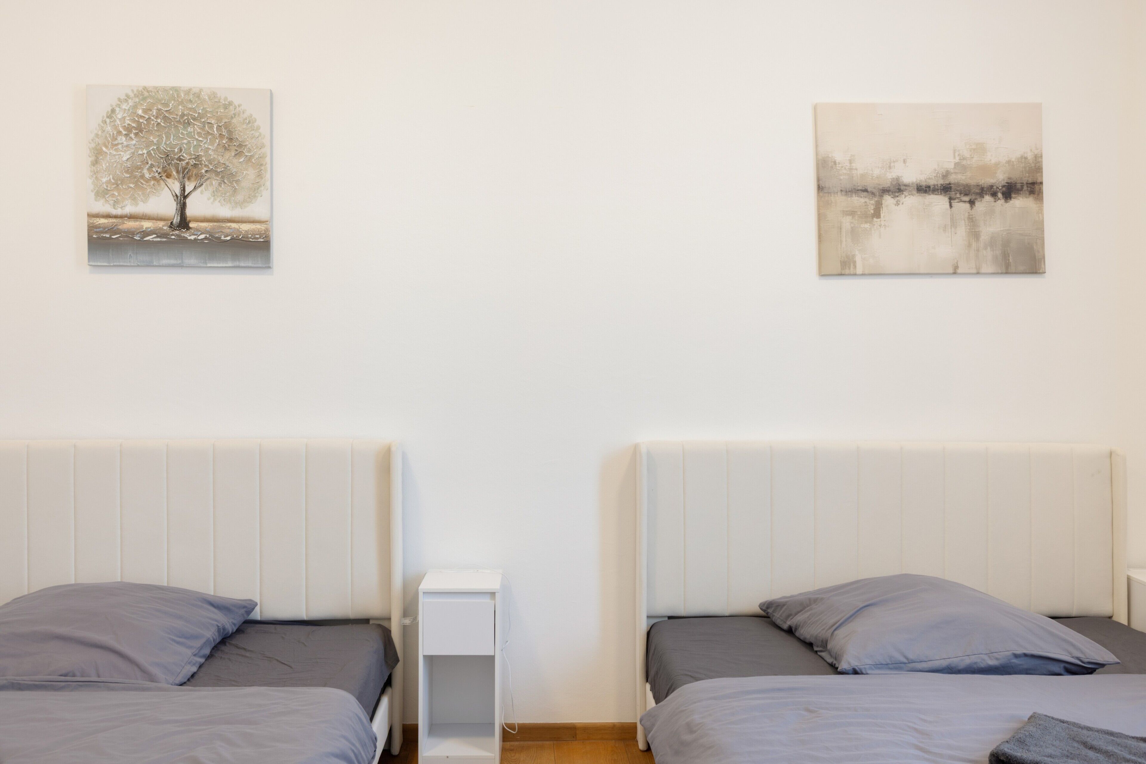 Une chambre avec deux lits, une table de chevet et deux tableaux accrochés au mur.