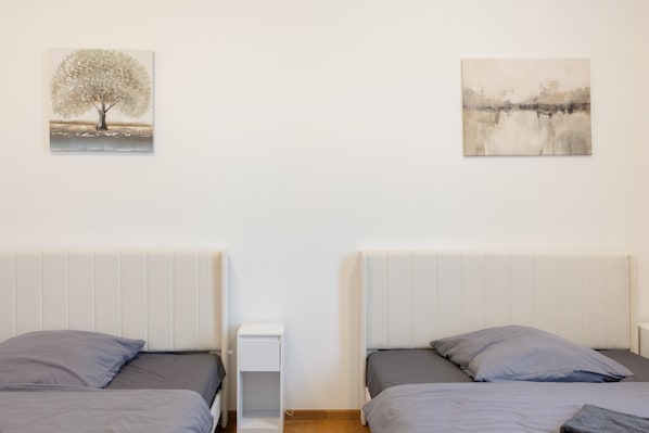 A bedroom with two beds, a bedside table, and two wall-mounted paintings.