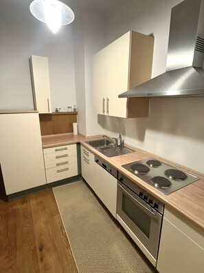 Moderni keittiö, jossa on valkoiset kaapit, ruostumattomasta teräksestä valmistettu liesi ja puinen työtaso.