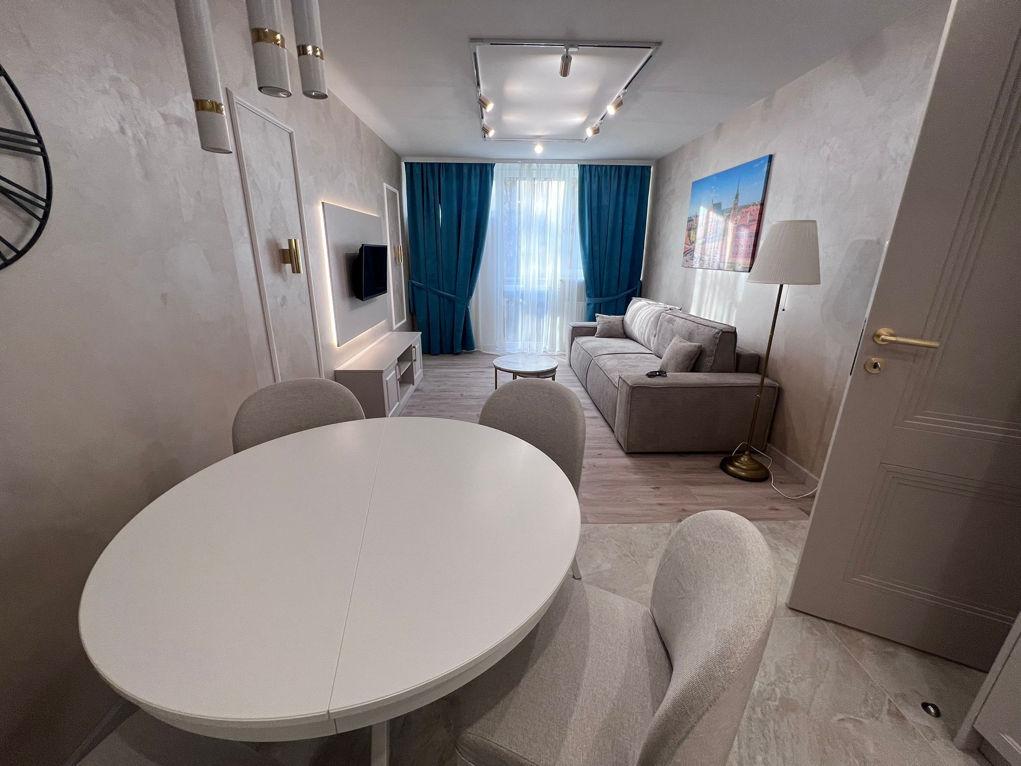 A modern hotel room with a round dining table, a sofa, and a TV mounted on the wall.