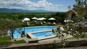 Une piscine entourée de chaises longues et de parasols, avec une végétation luxuriante et des montagnes en toile de fond.