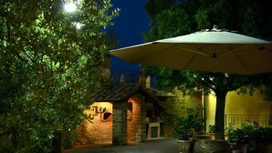 Un bâtiment en pierre avec un toit recouvert de tuiles, un grand parasol et des plantes en pot.