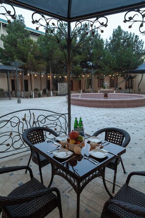 An outdoor patio with a round table and four chairs, surrounded by a decorative fence and trees. - Zarafshon Garden Hotel (Bukhara)