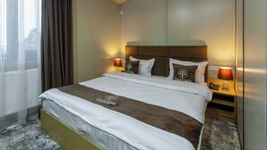 Ein Hotelzimmer mit einem großen Bett, zwei Nachttischlampen, einem Kopfteil und einem Fenster mit Vorhängen.