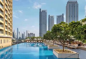 A swimming pool with lounge chairs and trees, surrounded by tall buildings. - Abi Holidays Dubai Mall Fashion Avenue  (Dubai)