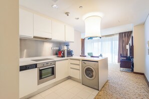 Eine moderne Küche mit Geschirrspüler, Backofen und Waschmaschine. Ein großes Fenster mit Vorhängen bietet einen Blick ins Freie.
