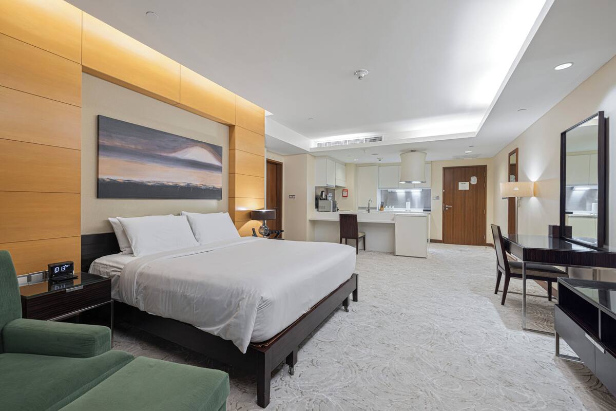 Ein Hotelzimmer mit einem großen Bett, einem Schreibtisch, einem Stuhl, einem Fernseher, einem Badezimmer und einer Küchenzeile.
