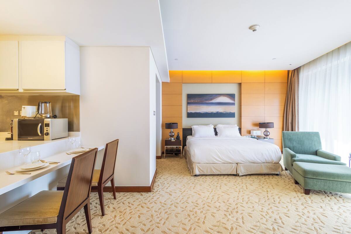 Ein Hotelzimmer mit einem Bett, einem Schreibtisch mit Stuhl, einer Mikrowelle, einem Wandbild und einem grünen Sessel.