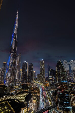 A nighttime cityscape with a prominent skyscraper, illuminated buildings, and busy streets. - Abi Holidays Dubai Mall Fashion Avenue  (Dubai)