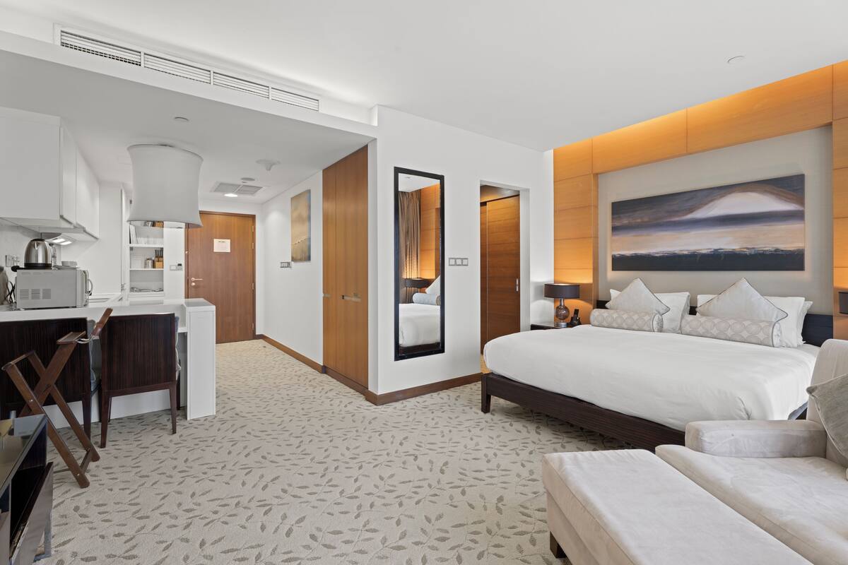 Ein Hotelzimmer mit einem großen Bett, einem Schreibtisch mit Stuhl, einer Küchenzeile und einem durch eine offene Tür einsehbaren Badezimmer.