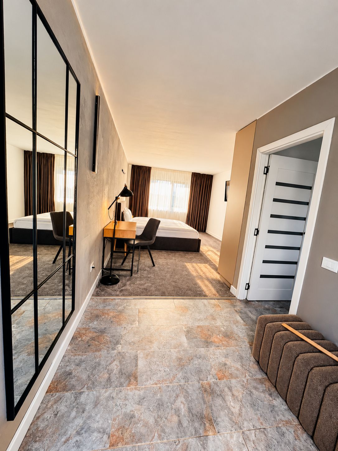 A hotel room with a bed, a desk, a chair, a mirror, and a wardrobe.