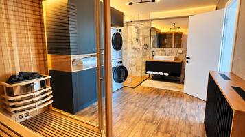Une salle de bain moderne dotée d’une douche à parois de verre, d’un lave-linge encastré et d’un banc en bois pour le sauna.