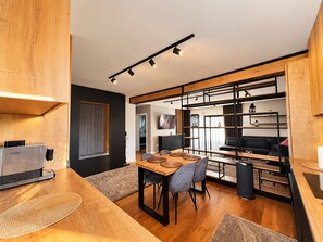 A modern kitchen with a dining area, wooden flooring, and built-in shelving.