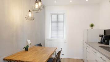 Une cuisine moderne avec une table en bois, des chaises, des luminaires suspendus, une fenêtre et une machine à café.