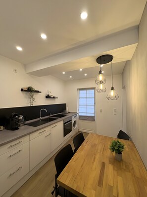 Una cocina moderna con una mesa de comedor de madera, electrodomésticos integrados e iluminación colgante.