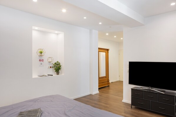 A modern bedroom with a bed, a TV, a dresser, and a mirror.