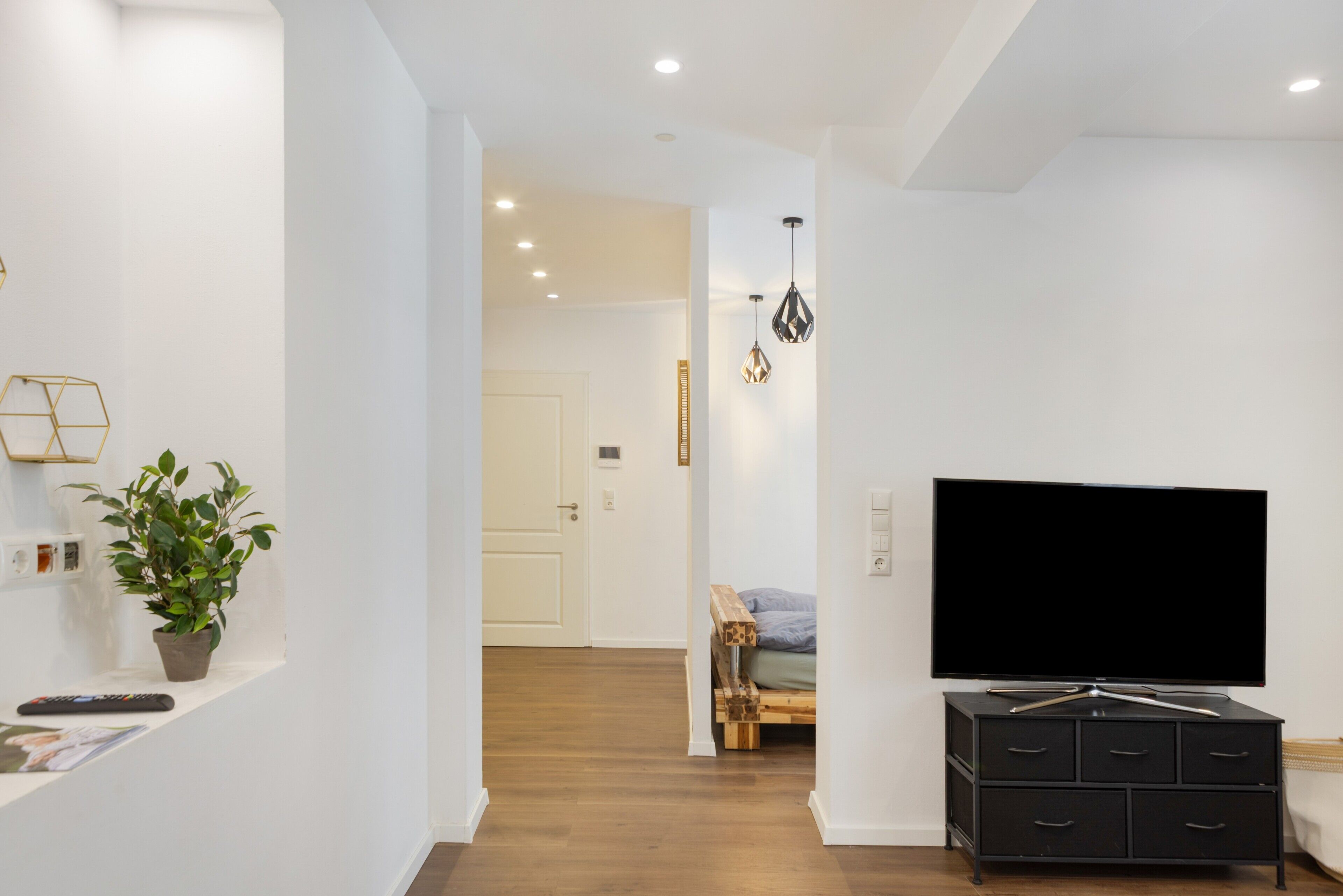 Een moderne woonkamer met een flatscreen televisie, een houten bankje en een potplant.