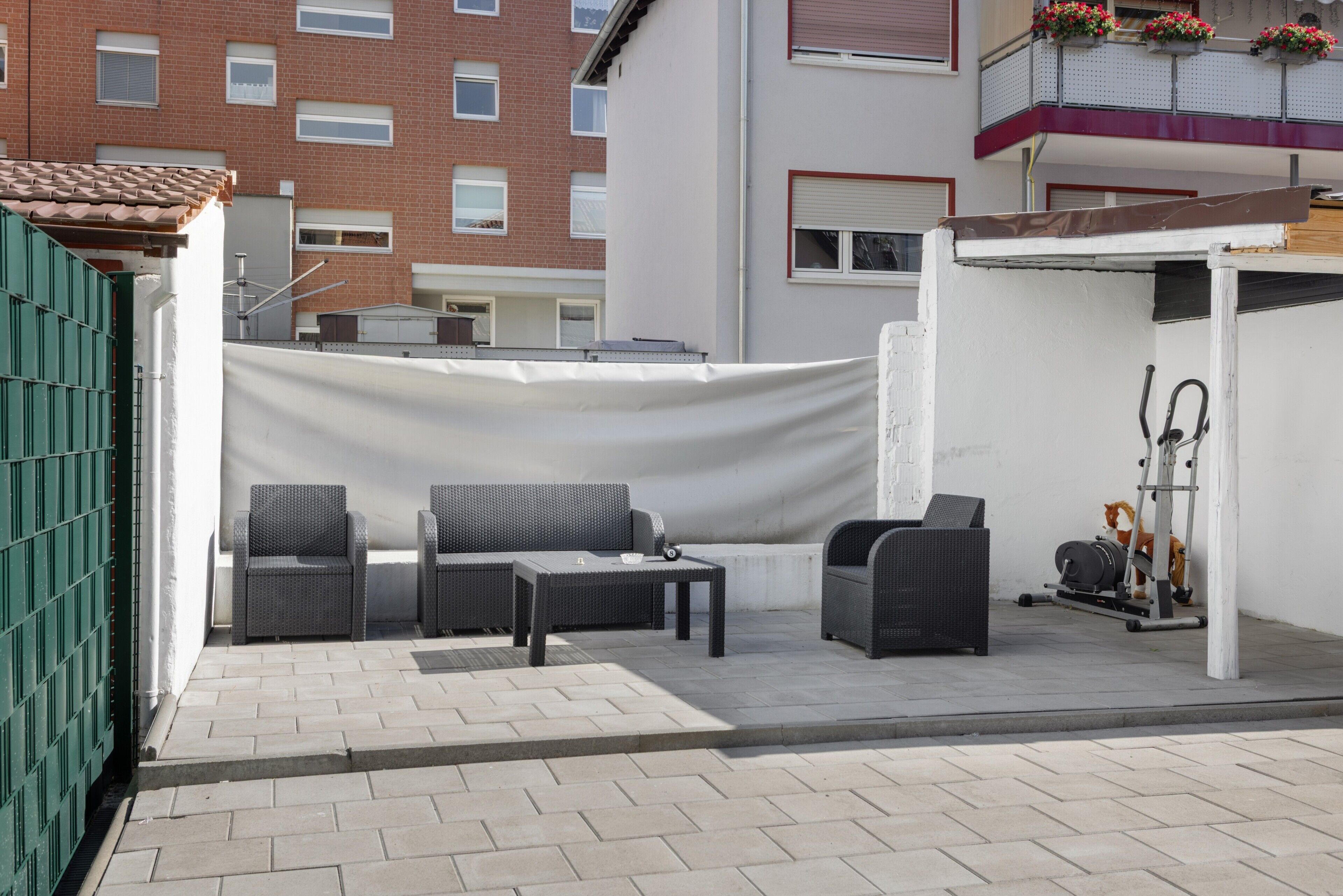Un espace extérieur aménagé avec un canapé, des fauteuils et une table, une terrasse couverte et une salle de sport équipée de matériel d’exercice.