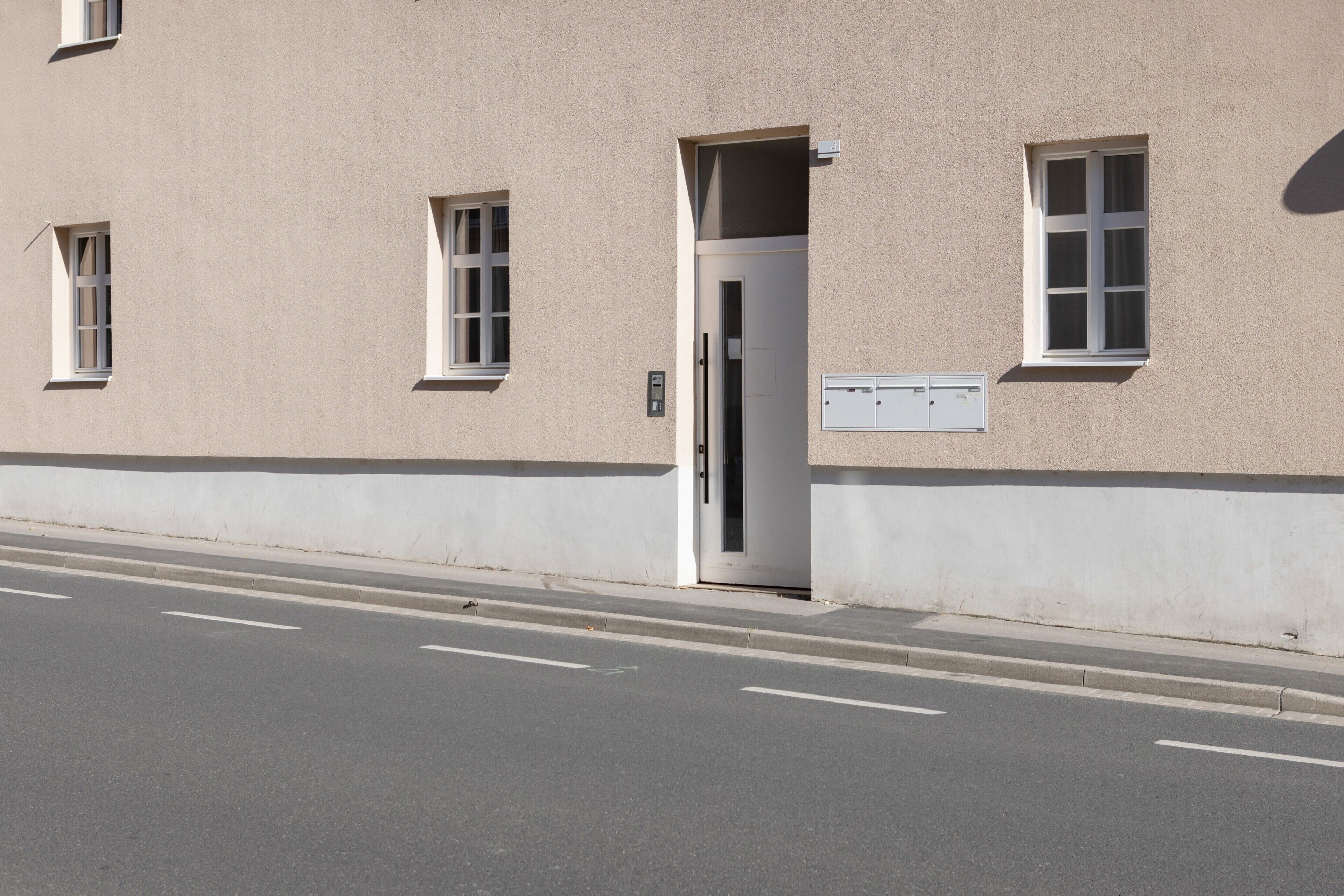 Ein Gebäude mit einer beige farbenen Fassade, einer weißen Tür und einem kleinen Fenster mit der Aufschrift '4'.